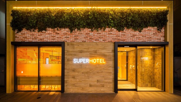 A hotel entrance with a brick facade, a neon sign, and a green plant-covered ledge above the entrance.