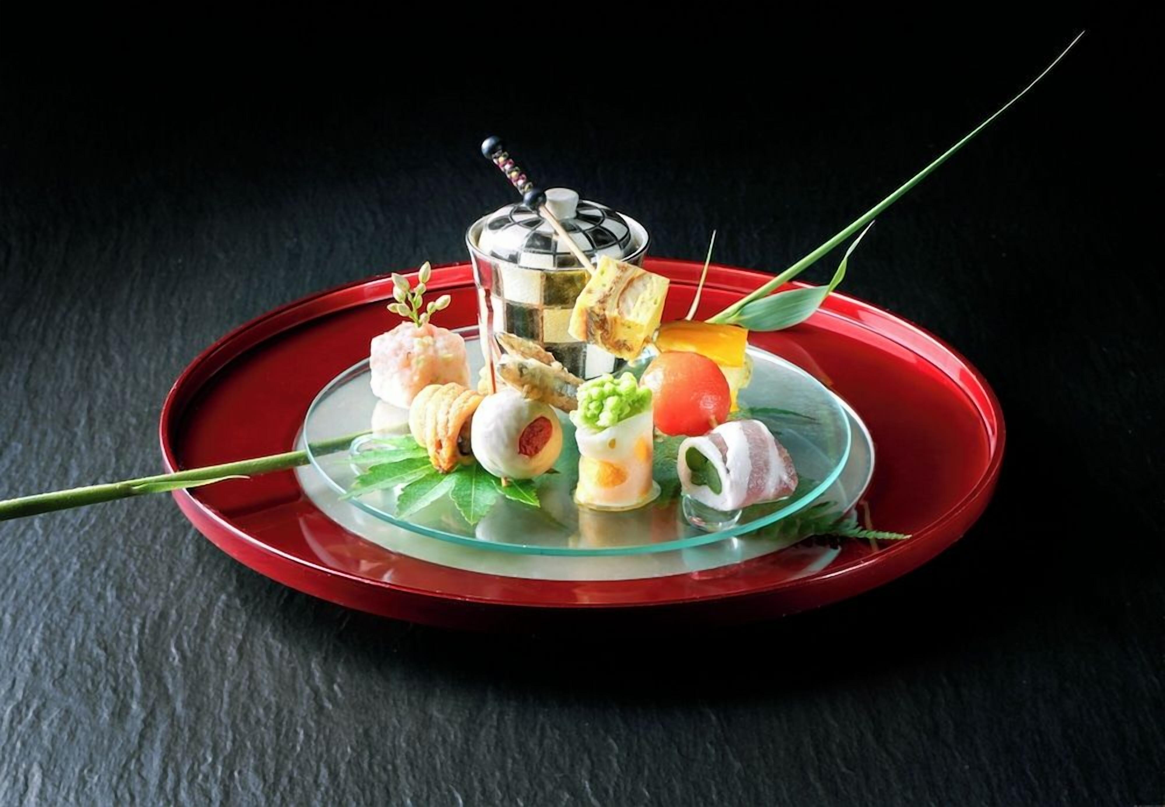 A glass plate with various food items, including shrimp, a roll, and a small dish with a lid.