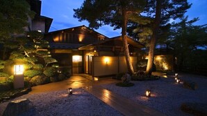 A traditional Japanese-style house with a wooden exterior, a well-maintained garden, and a gravel driveway. - Dokutsuburo no Yado Hyakurakuso (Noto)