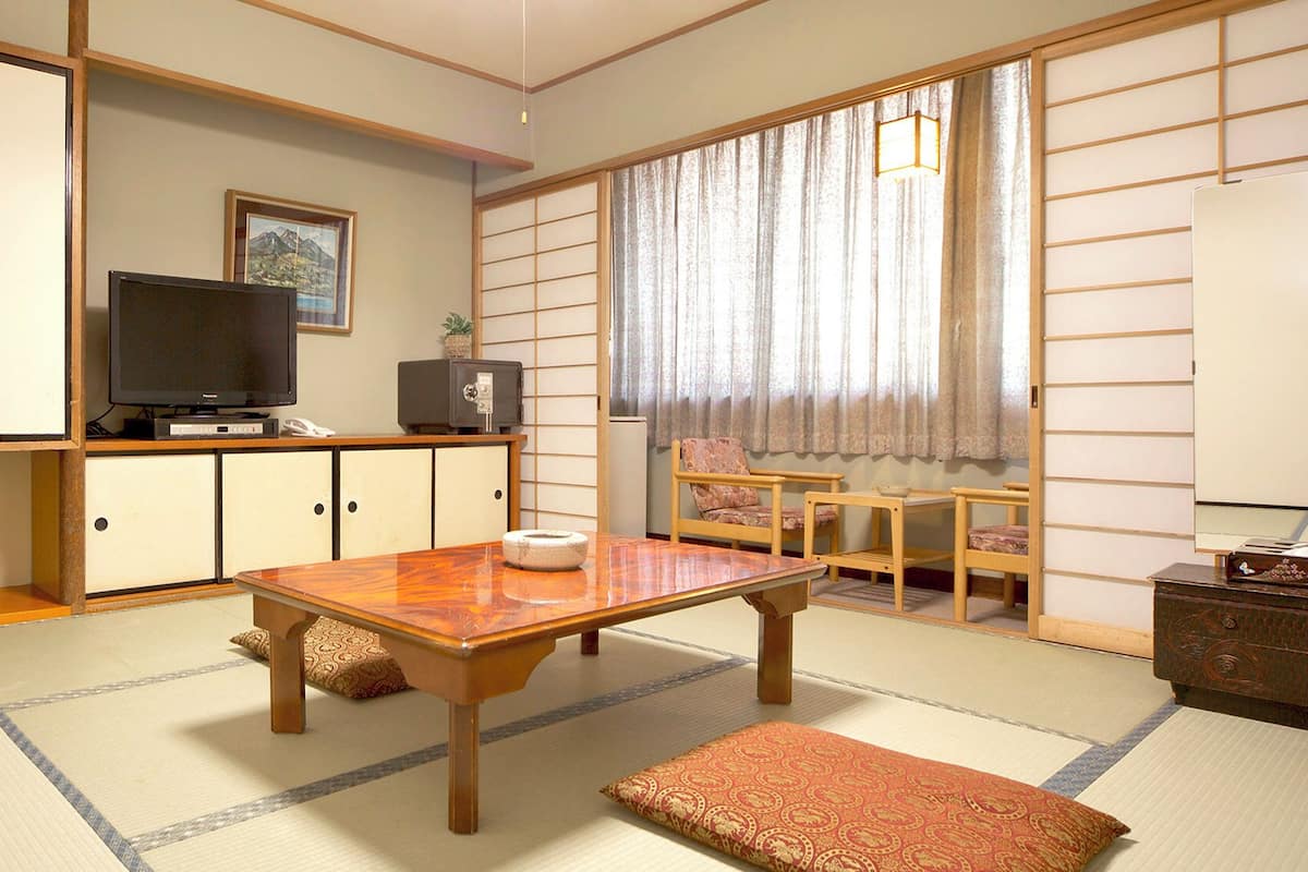 A traditional Japanese room with tatami flooring, a low table, a television, and sliding doors.