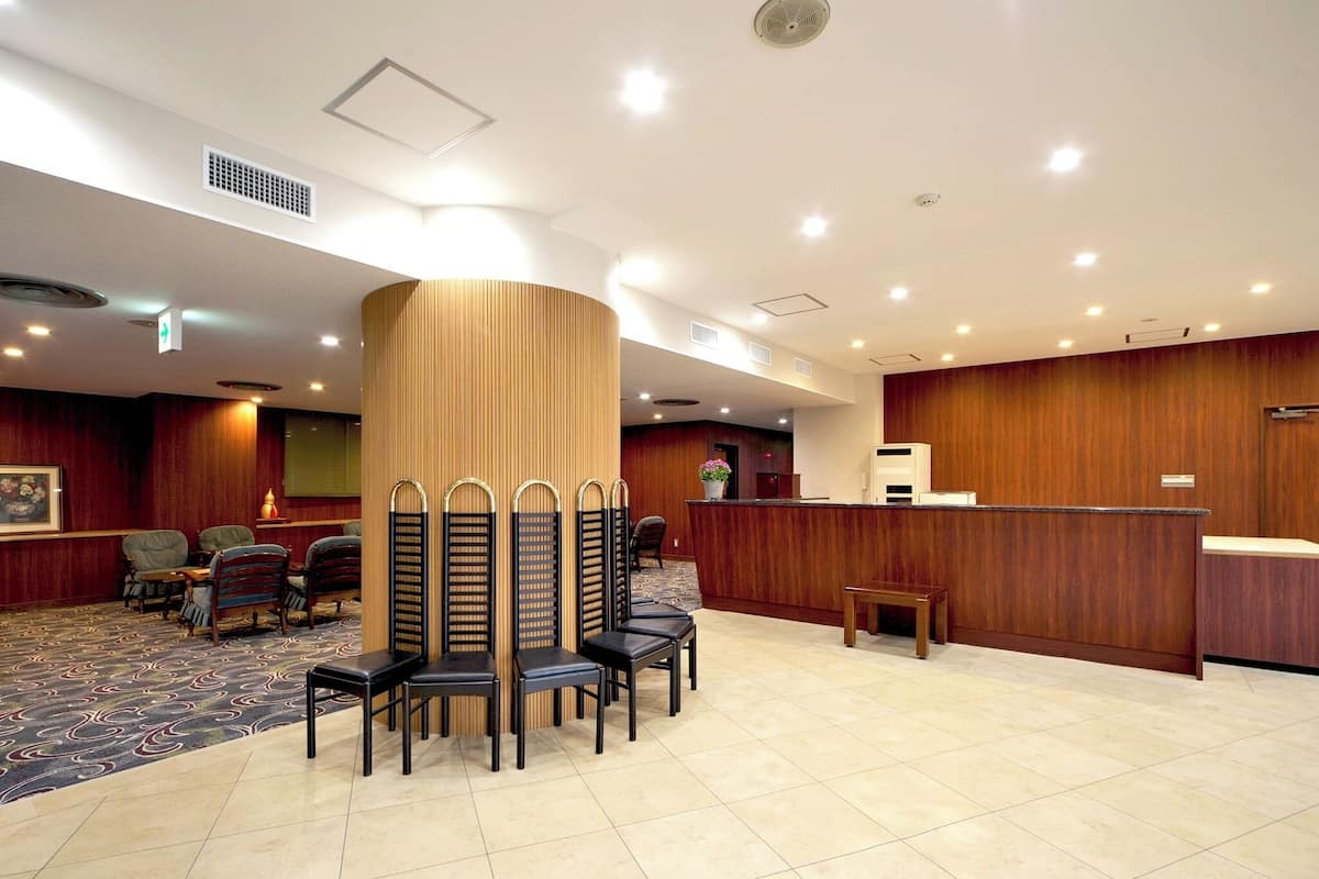 A hotel lobby with a reception desk, seating area with chairs, a patterned carpet, and a large pillar.