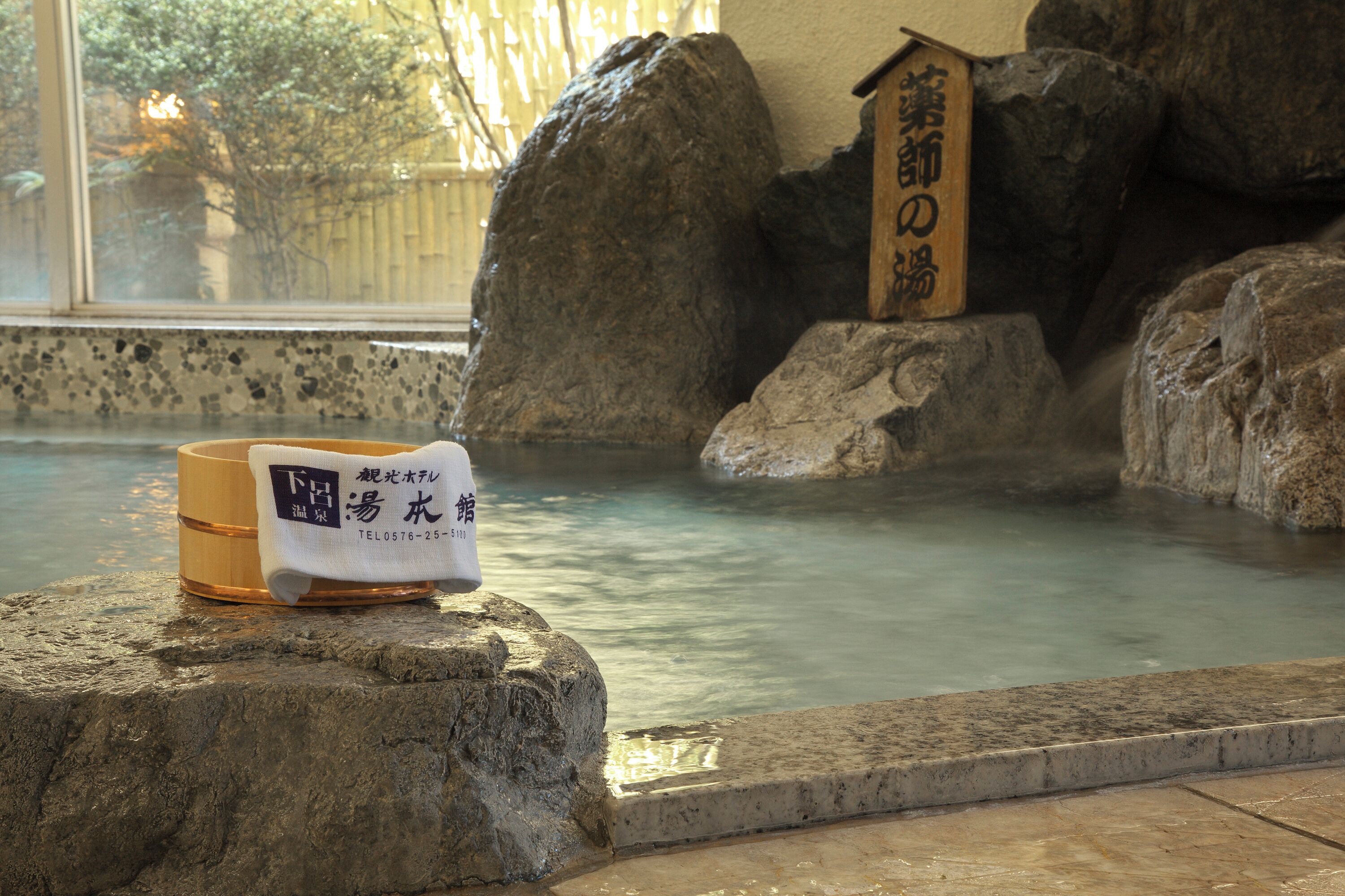 A stone bath with a wooden sign, a towel, and a cup with Japanese text.