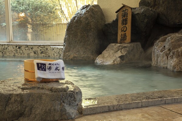 A stone bath with a wooden sign, a towel, and a cup with Japanese text.