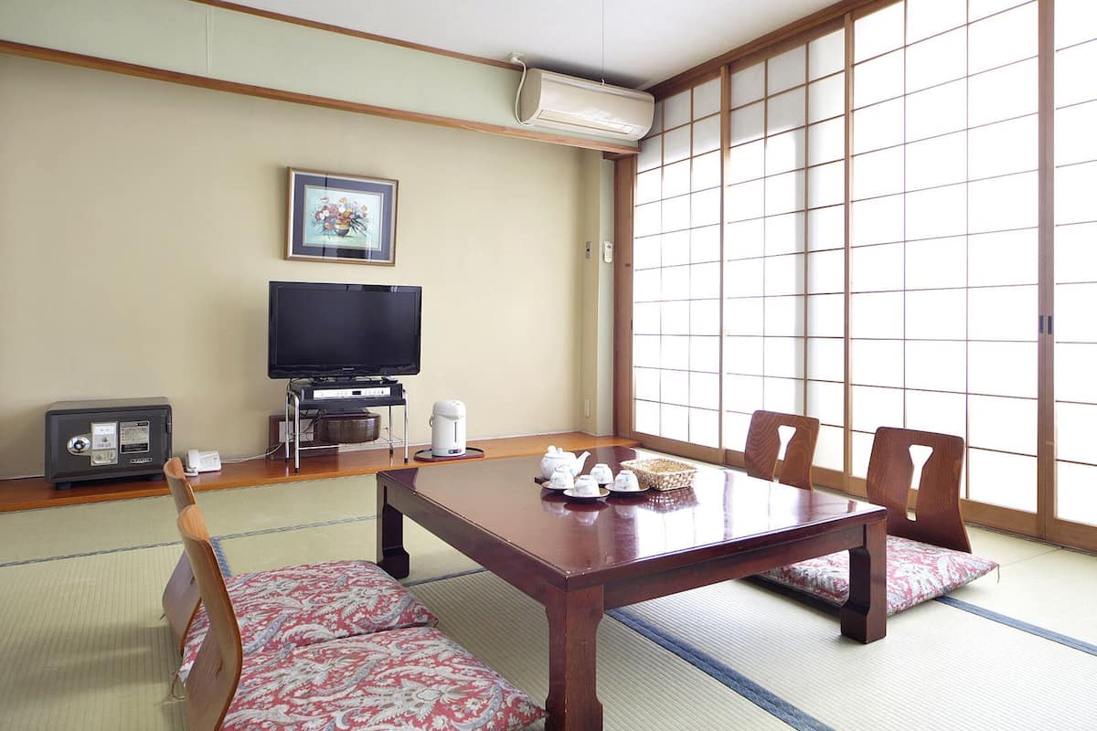 A traditional Japanese room with tatami flooring, a low table with a tea set, a television, and a futon bed.