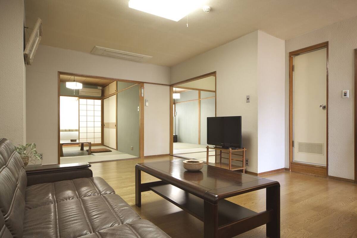 A living room with a sofa, a coffee table, a television, and a sliding door leading to a traditional Japanese room.
