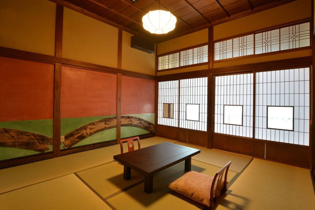 Ein traditioneller japanischer Raum mit Tatami-Böden, einem niedrigen Tisch und verschiebbaren Türen mit dekorativen Mustern.