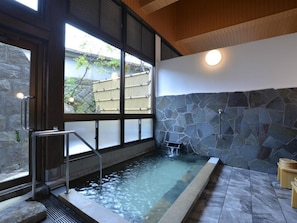 Un área de spa con pared de piedra, una bañera de hidromasaje y una ventana con vistas a una valla de bambú.
