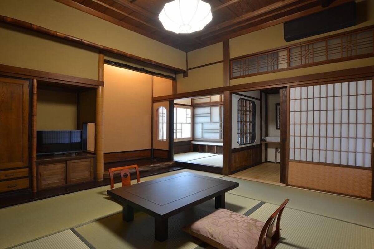 Ein traditioneller japanischer Raum mit Tatami-Böden, einem niedrigen Tisch, einem Fernseher und Schiebetüren.