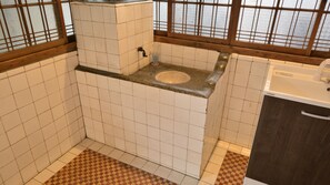 A compact bathroom with a toilet, sink, and a window with a grid pattern. - Yoshino Ryokan (Hitoyoshi)