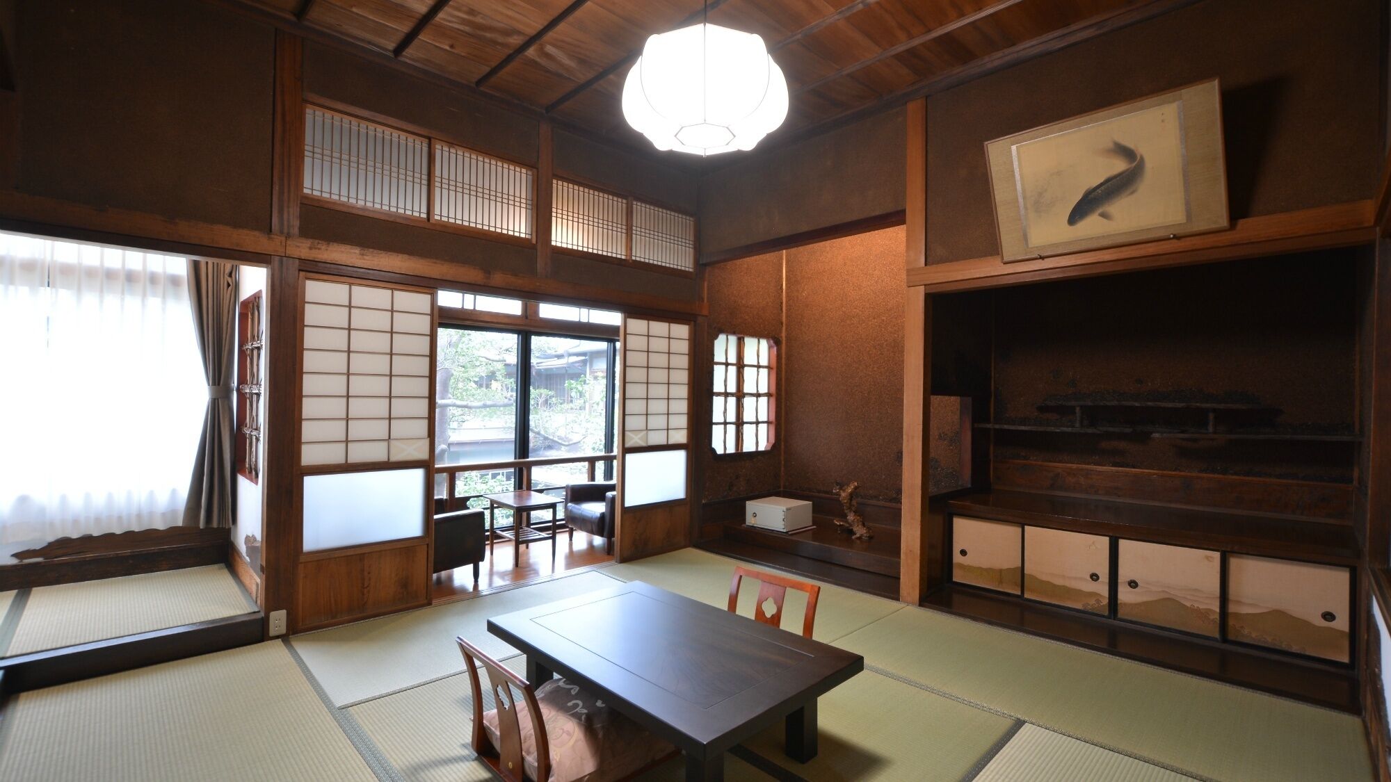 Une pièce de style japonais traditionnel, avec un sol recouvert de tatamis, une table basse, des chaises, des portes coulissantes en papier de riz (shoji) et un luminaire au plafond.