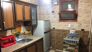 Une cuisine de taille réduite, dotée de meubles en bois, d’un réfrigérateur en acier inoxydable, d’une cuisinière à gaz et d’un évier.