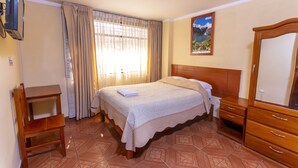 A bedroom with a bed, wooden dresser, bedside table, and a television mounted on the wall. - Hotel Tamia (Huaraz)