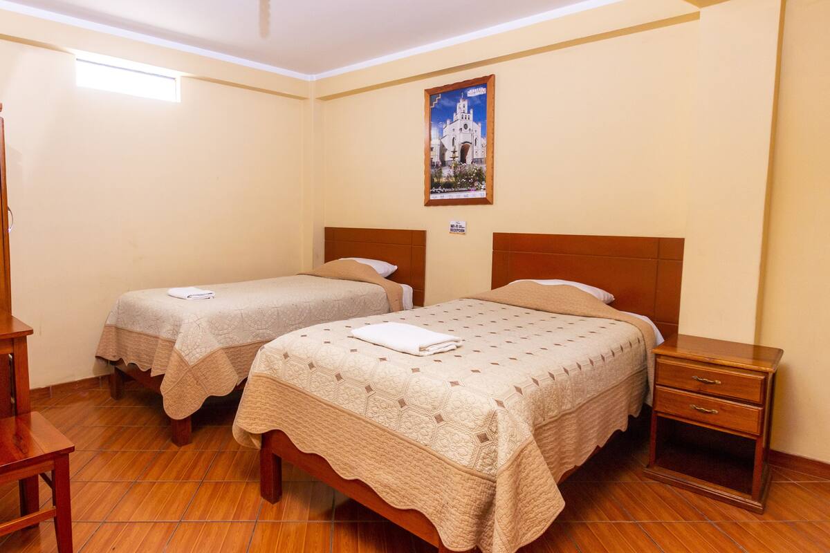 A hotel room with two single beds, a wooden nightstand, a wooden wardrobe, and a wall-mounted picture.