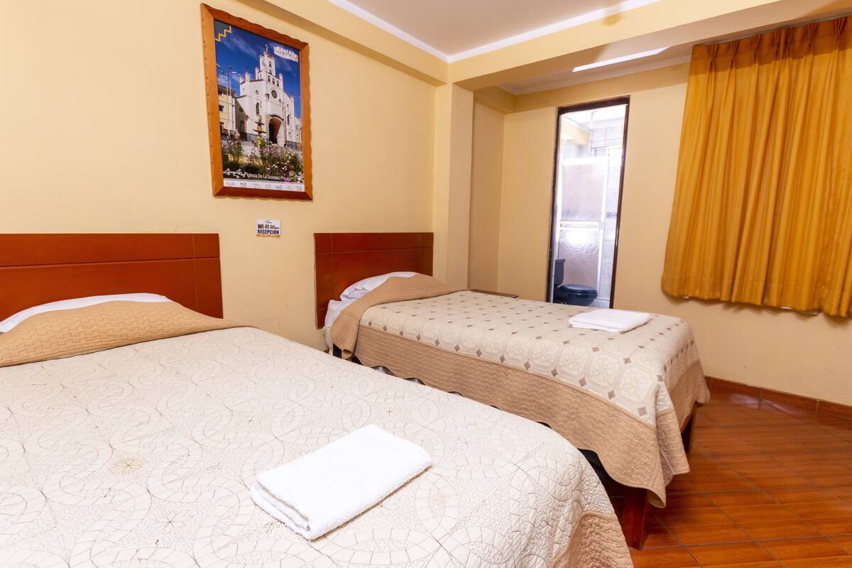 A hotel room with two beds, a wooden headboard, a poster on the wall, and a bathroom door.
