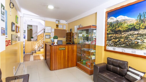 A reception area with a wooden counter, a glass display case, and a large framed picture of a mountain landscape. - Hotel Tamia (Huaraz)