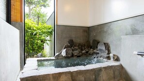 Un espace de bien-être avec un bain à remous en pierre, entouré de rochers, et offrant une vue sur la verdure environnante.
