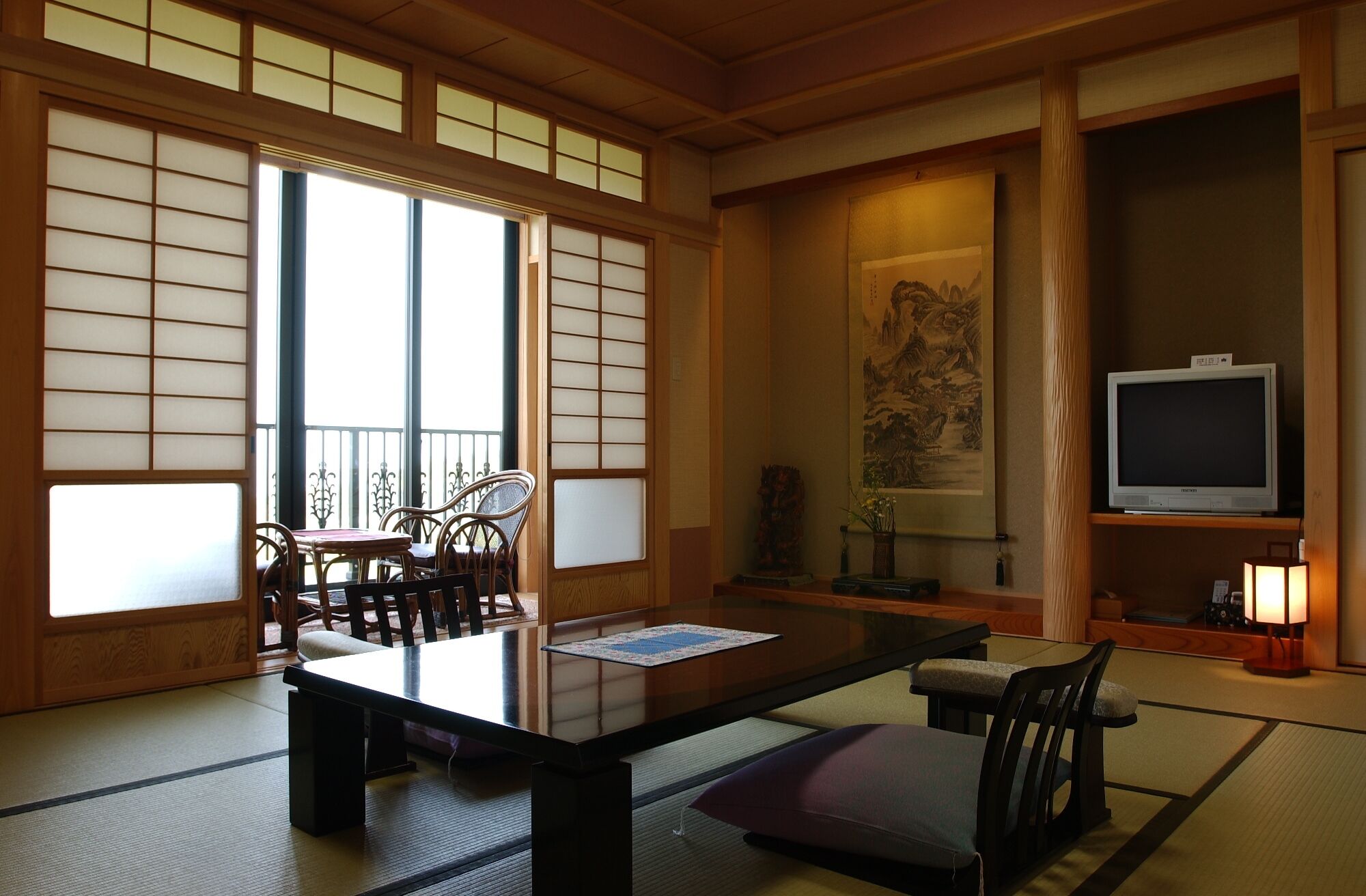 Une pièce de style japonais traditionnel, avec un sol recouvert de tatamis, une table basse, des chaises, un téléviseur et un tableau accroché au mur.