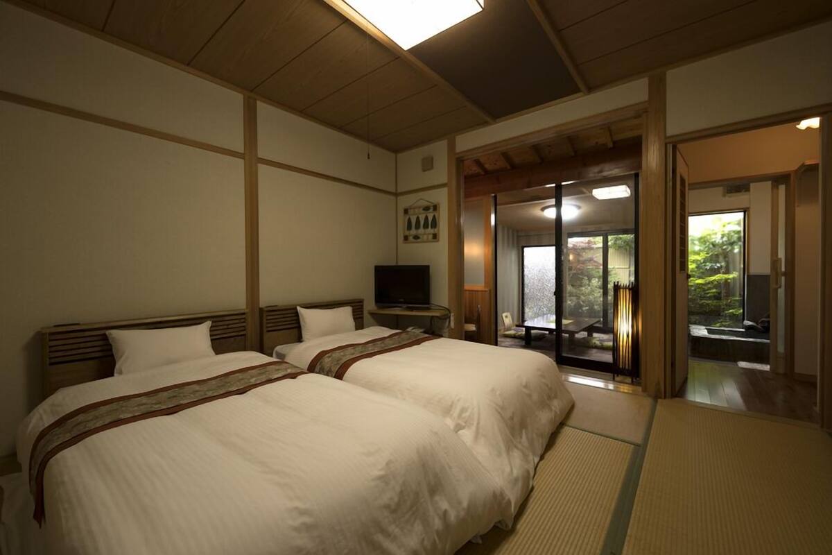 A hotel room with two beds, a television, a sliding door leading to a balcony, and tatami flooring.