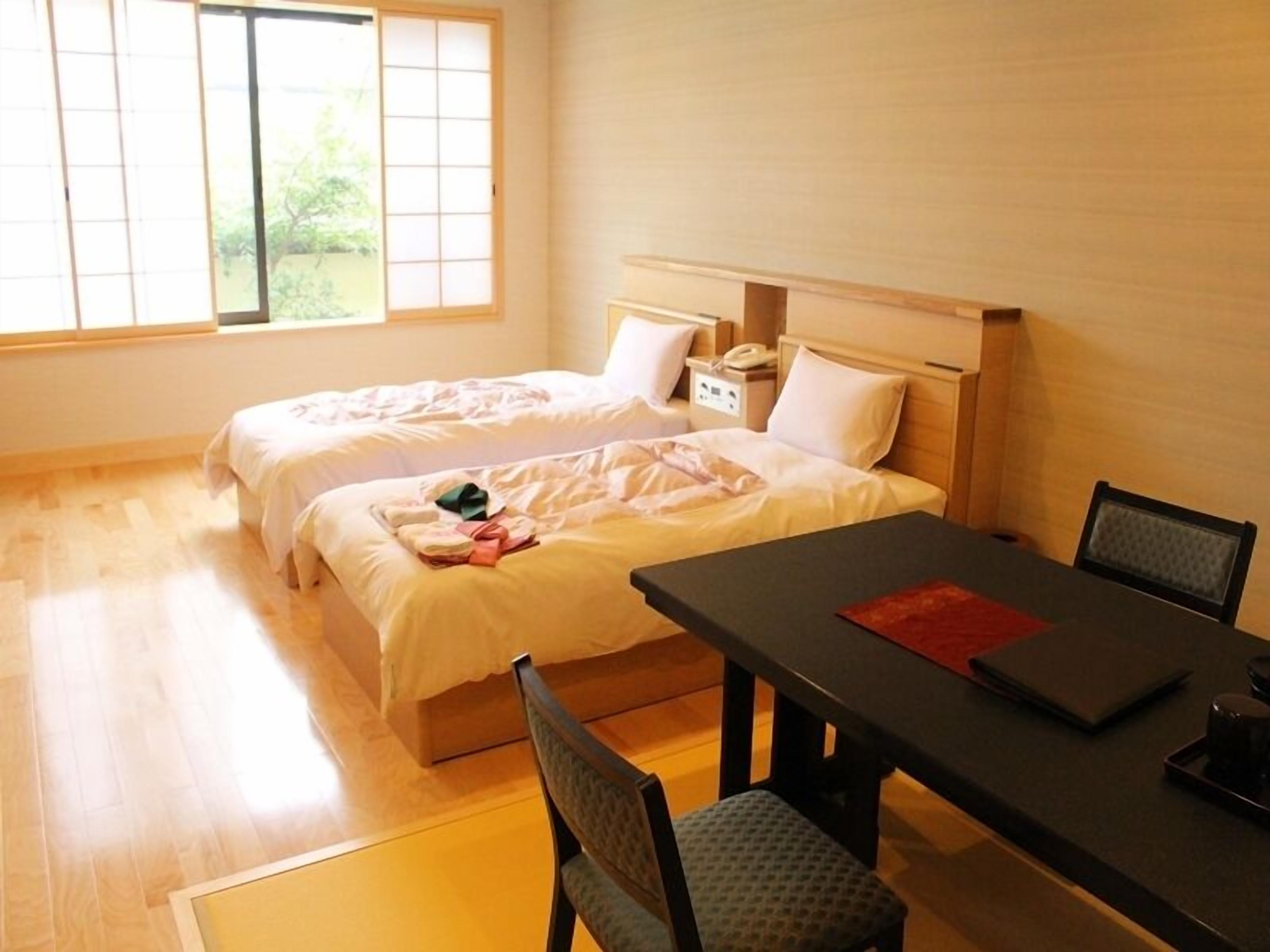 Une chambre d’hôtel avec deux lits, une table à manger et une vue sur la verdure environnante.