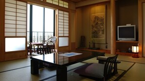 A traditional Japanese room with tatami flooring, a low table, chairs, a television, and a painting on the wall. - Ryotei Saigetsuan (Hirado)