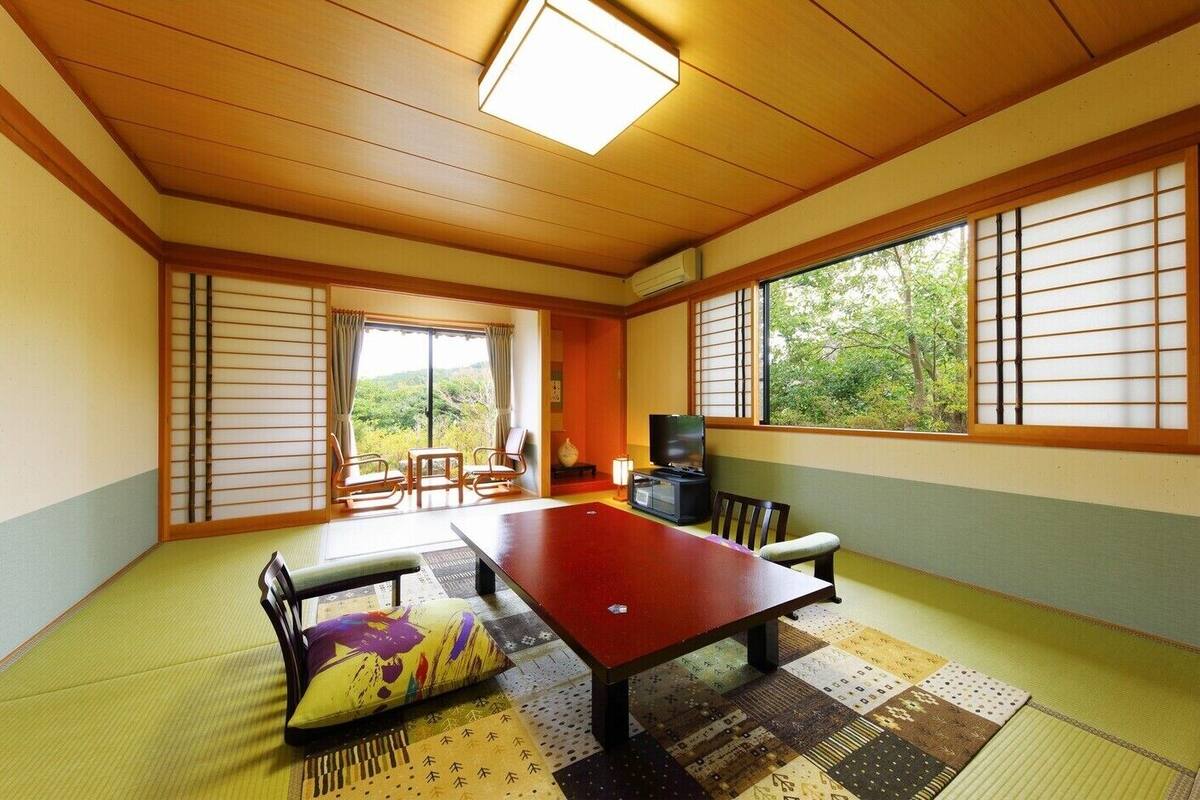 A traditional Japanese room with tatami flooring, a low table, chairs, and a television.