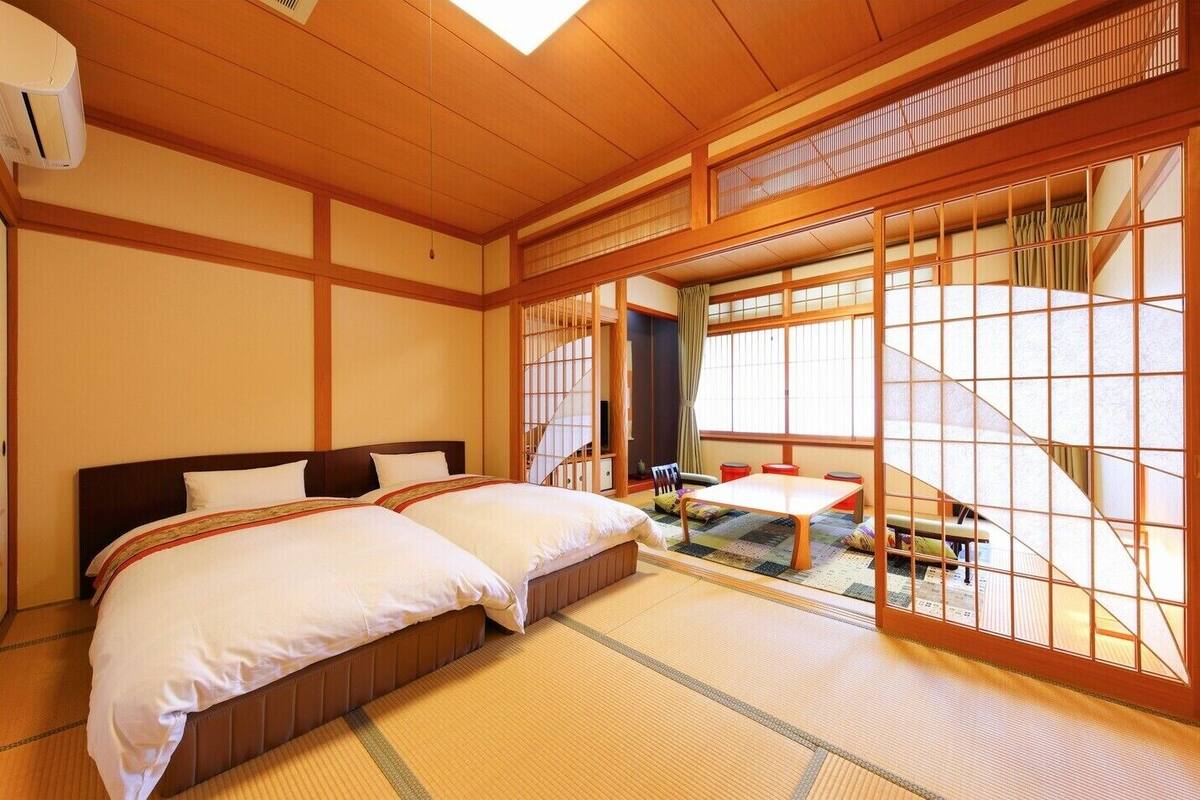A traditional Japanese-style room with tatami flooring, a bed with white bedding, a sliding door, and a small table with stools.