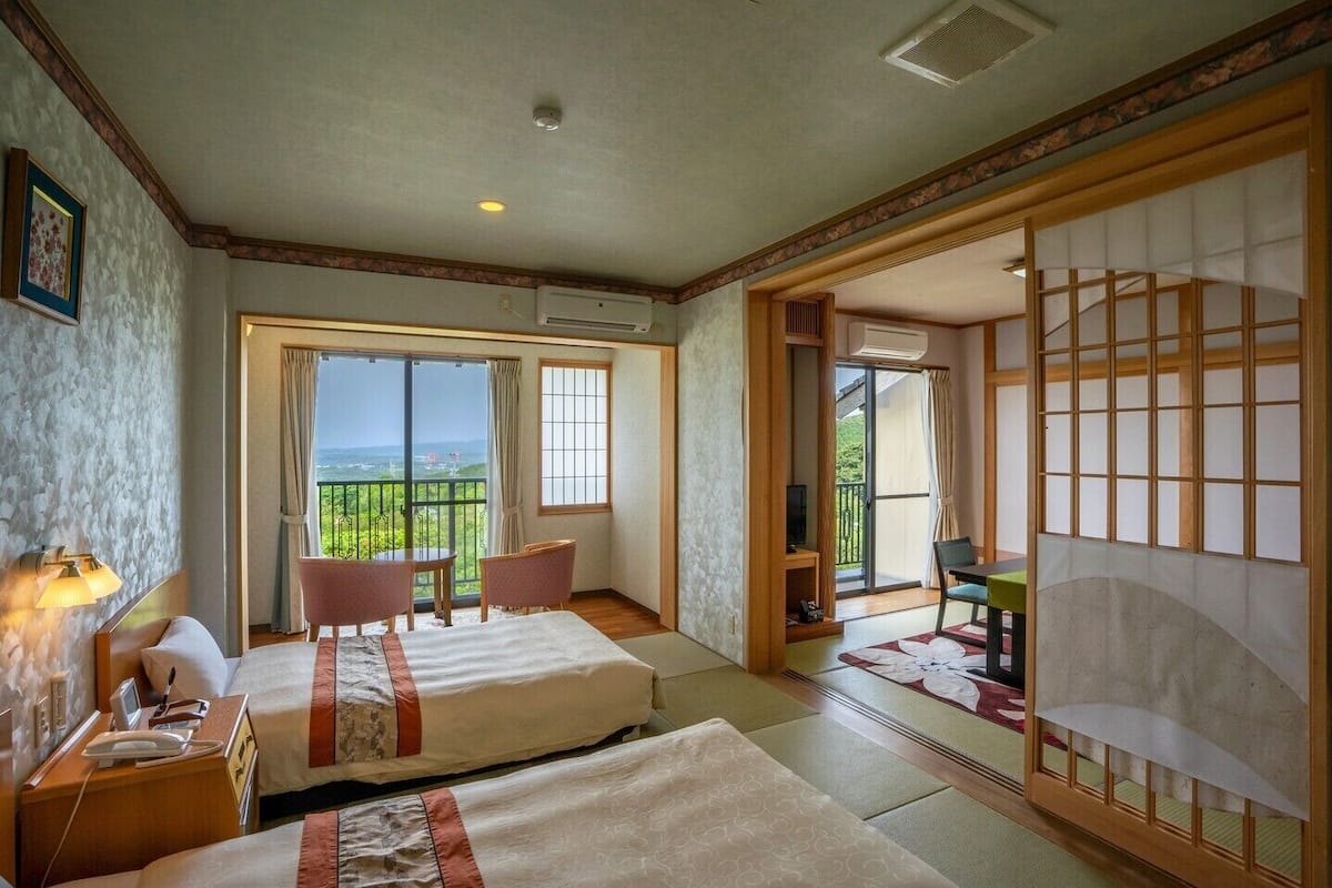 A hotel room with two beds, a balcony with a view, and traditional Japanese sliding doors.