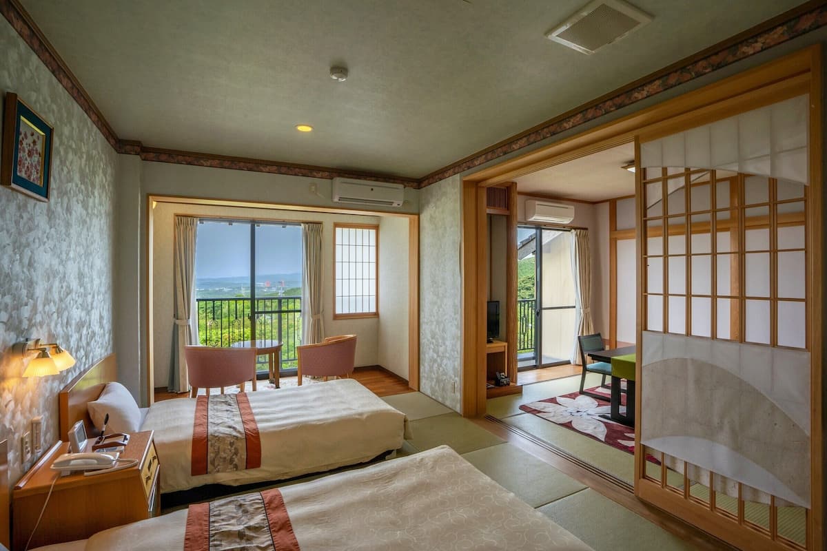 A hotel room with two beds, a balcony, a TV, and a traditional Japanese sliding door.