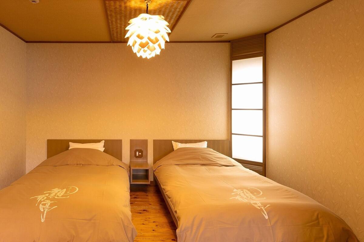 A room with two beds, a ceiling light, a window, and a door.