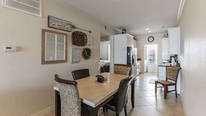 Un coin repas avec une table et des chaises en bois, une horloge au mur et une cuisine en arrière-plan.