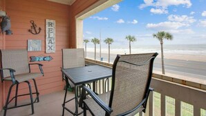Un balcon avec vue sur la plage, comprenant une table et des chaises, ainsi que des éléments décoratifs sur les murs.