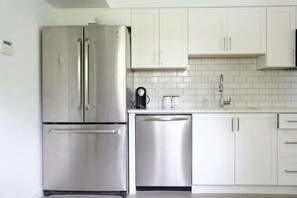 A kitchen with stainless steel appliances, white cabinets, and a tiled backsplash. - Kitsilano Modern Comfort - Spacious 1 bedroom in quiet tree lined neighbourhood (Vancouver)
