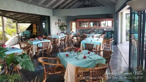 Un restaurante con varias mesas, sillas de mimbre y un fondo de pared de piedra.
