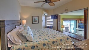 Un dormitorio con cama, ventilador de techo, ventana con persianas y vista al exterior.