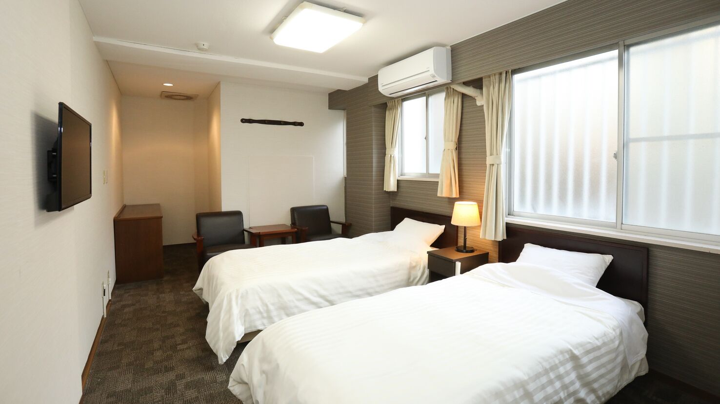 Habitación de hotel con dos camas, televisión, escritorio, silla y aire acondicionado.