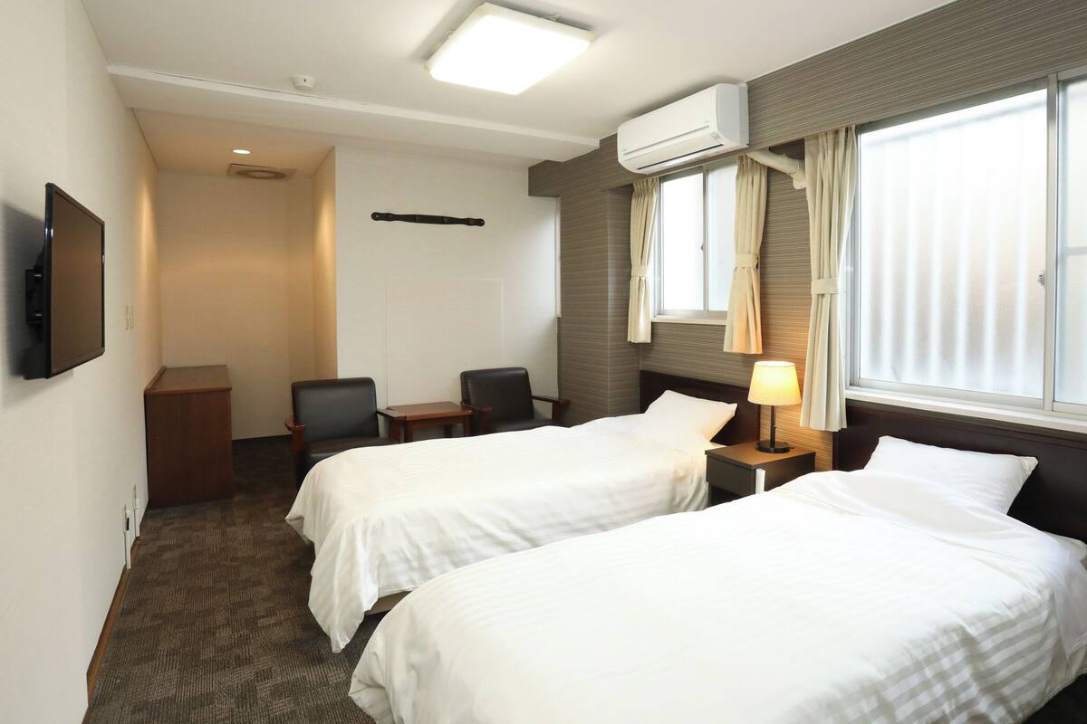 Habitación de hotel con dos camas, un escritorio, una silla, un televisor y un equipo de aire acondicionado.