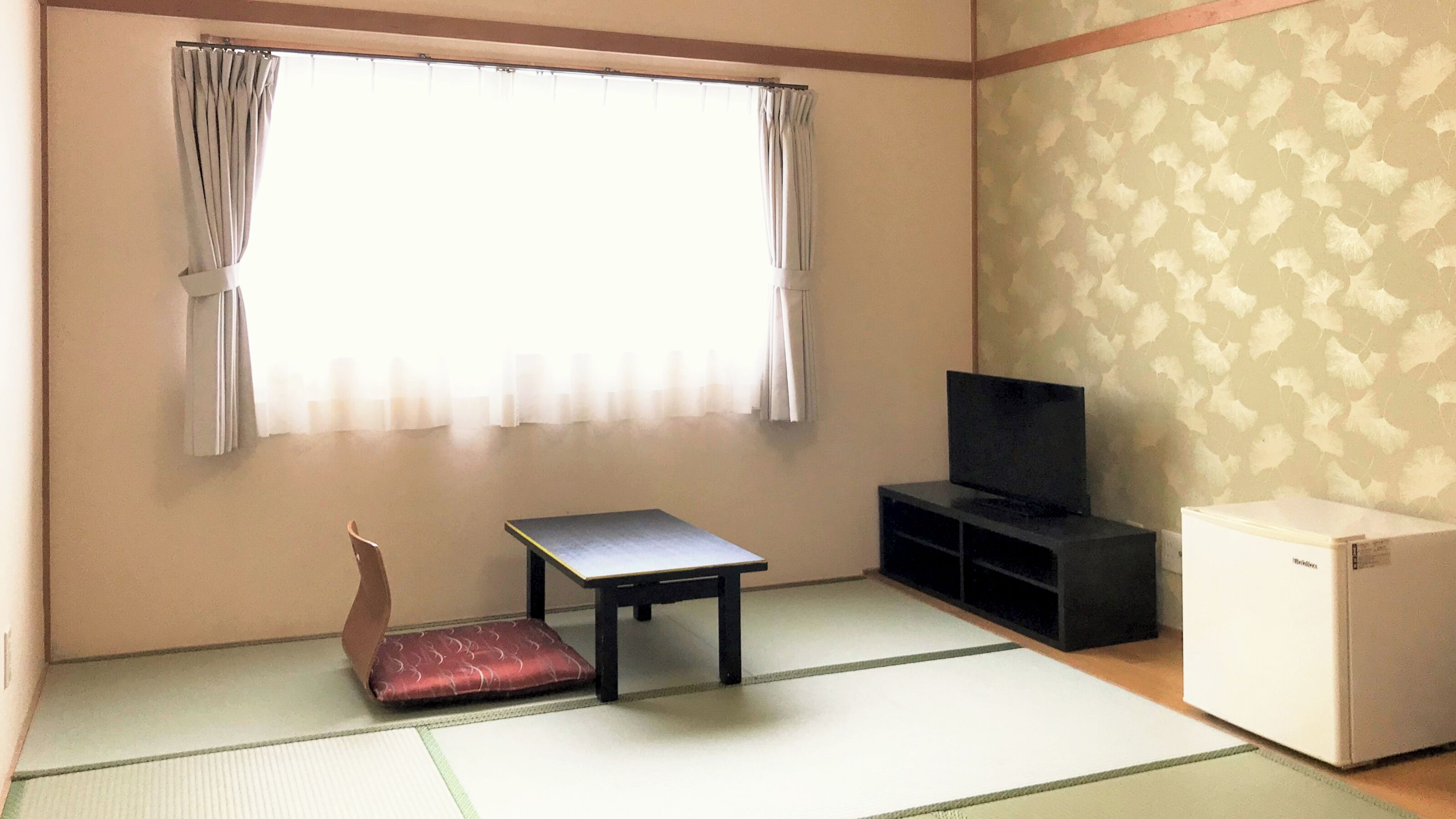 Una habitación con suelo de tatami, una mesa baja, un televisor y un refrigerador.