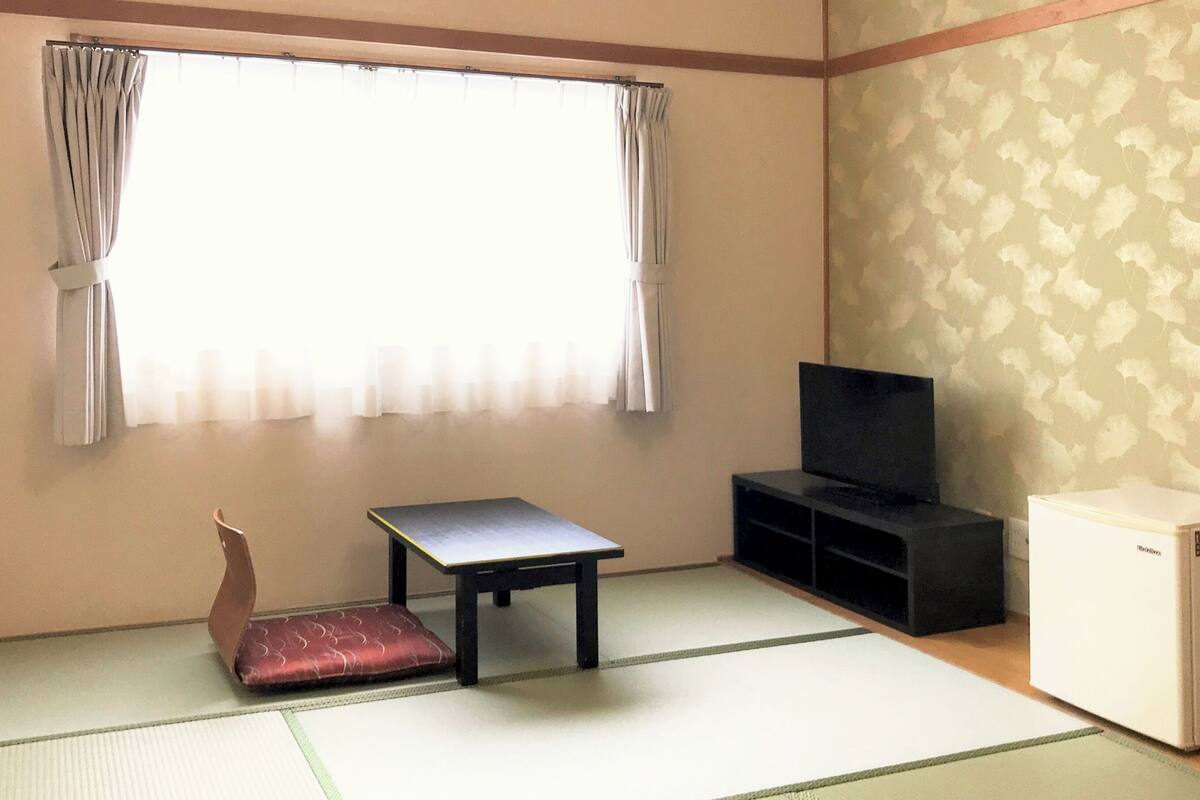 Una habitación con suelo de tatami, una mesa baja, un televisor y un refrigerador.