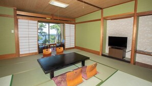 A traditional Japanese room with tatami flooring, a low table, cushions, a television, and a sliding door leading to a balcony. - Itoen Hotel Inatori (Higashiizu)