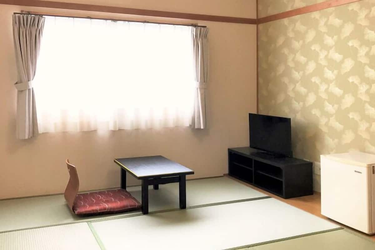 Una habitación con suelo de tatami, una mesa baja, un sofá, un televisor y un mueble pequeño.