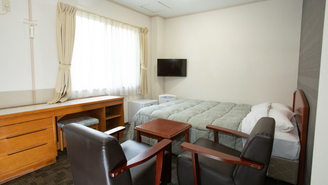 Habitación de hotel con cama, escritorio, silla, televisor y ventana con cortinas.