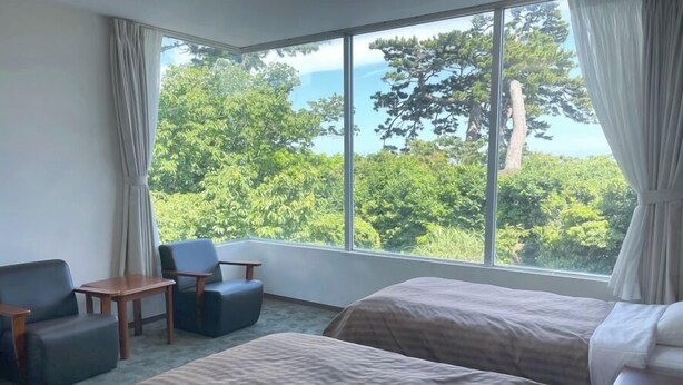 A hotel room with a large window, a bed, a chair, and a small table. - Itoen Hotel Inatori (Higashiizu)