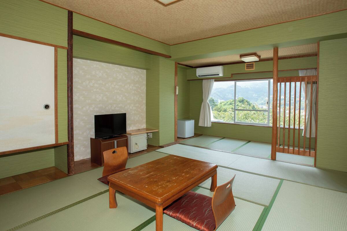 Una habitación japonesa tradicional con suelo de tatami, una mesa de madera, un televisor y una puerta corredera con vistas.