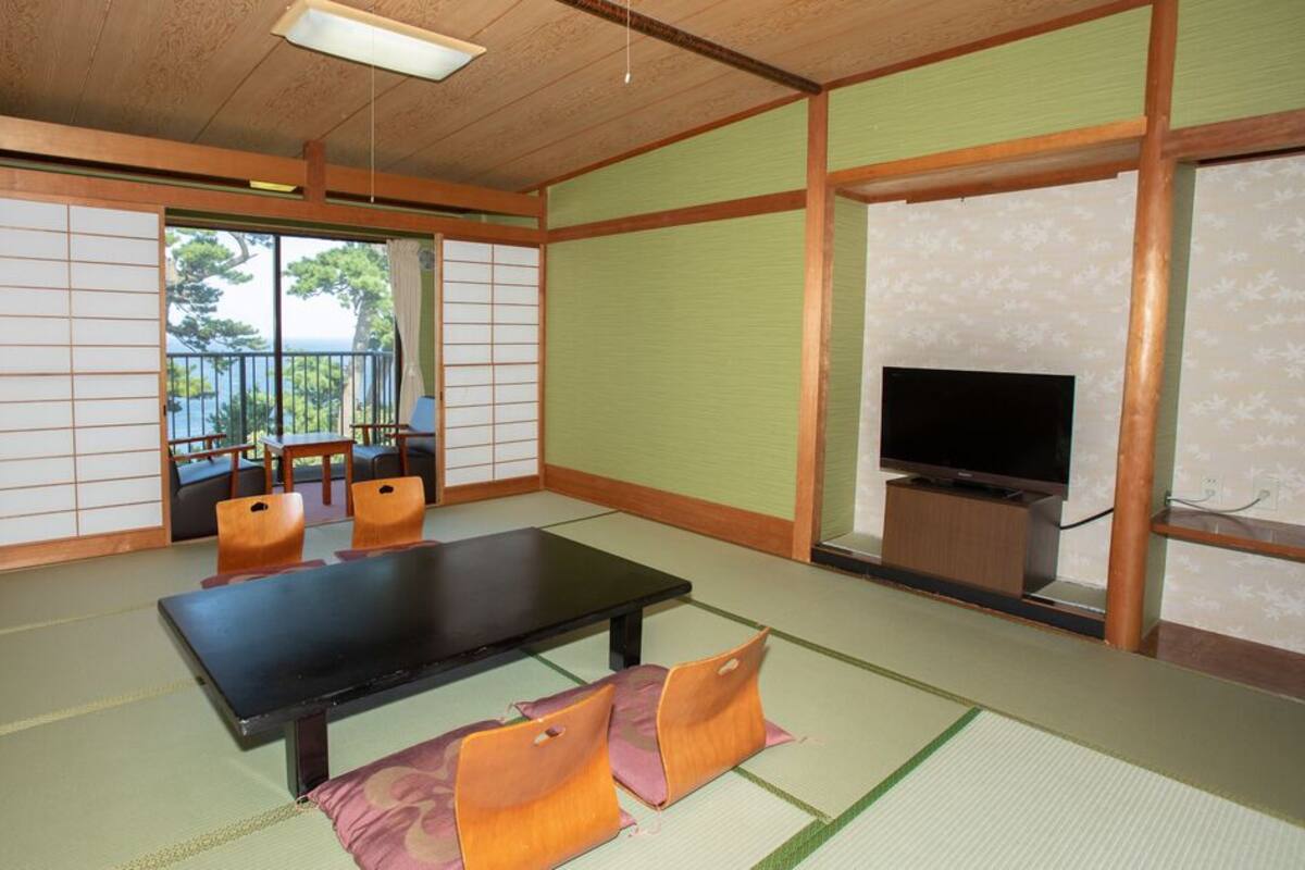 Una habitación con tatami, una mesa negra, cojines naranjas, un televisor y puertas correderas.
