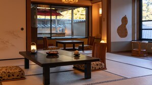 Una habitació japonesa tradicional amb paviment de tatami, una taula baixa amb un bol i una espelma, i vista d'un edifici tradicional a l'exterior.