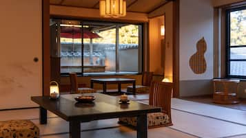 A traditional Japanese room with tatami flooring, a low table with a bowl and a candle, and a view of a traditional building outside.