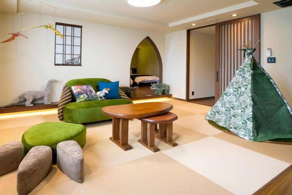 Un salon moderne avec un canapé vert, deux poufs, une table basse en bois et une plante suspendue.