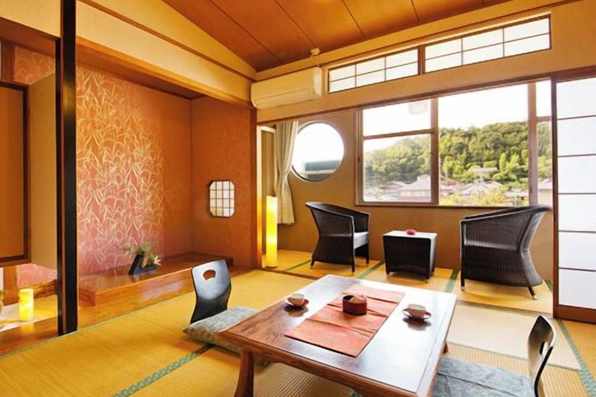 Une pièce de style japonais traditionnel, avec un sol recouvert de tatamis, une petite table basse avec un service à thé, et une vue sur une forêt à travers de grandes fenêtres.