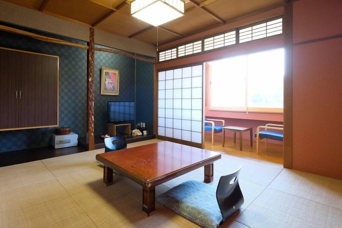 Une pièce de style japonais traditionnel, avec un sol recouvert de tatamis, une table basse, un téléviseur et des portes coulissantes.