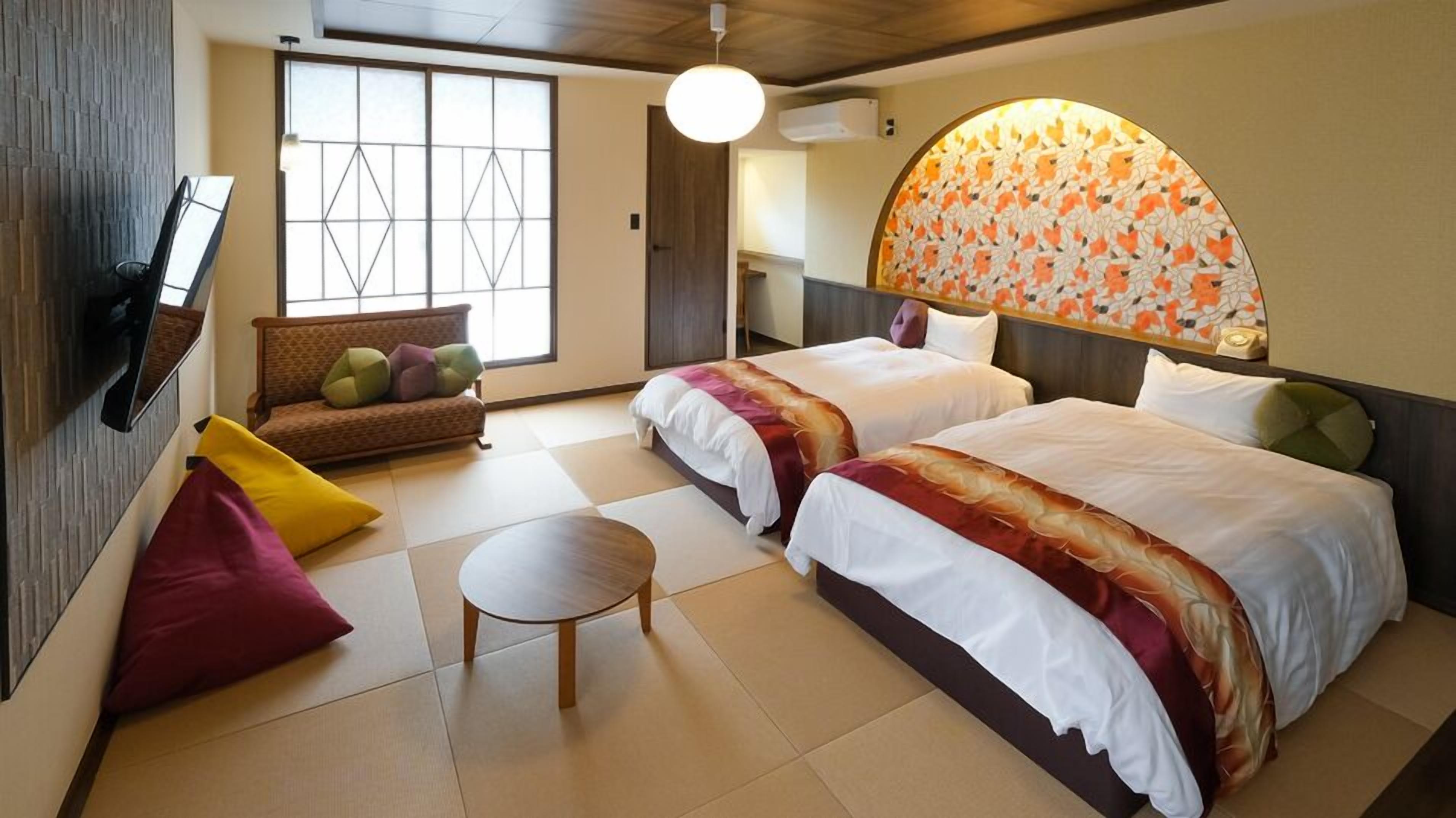 A hotel room with two beds, a sofa, a small table, and a large window with a view.